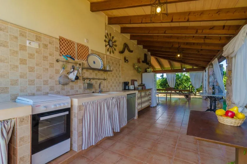Una cocina exterior cubierta y zona de comedor con una encimera larga y vigas de madera.