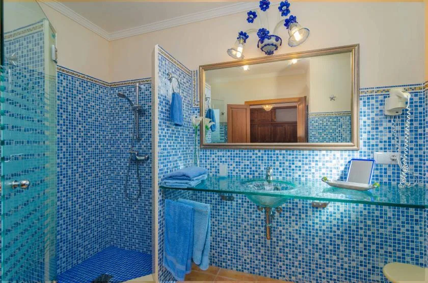Un baño alicatado con encimera de vidrio, espejo y ducha.