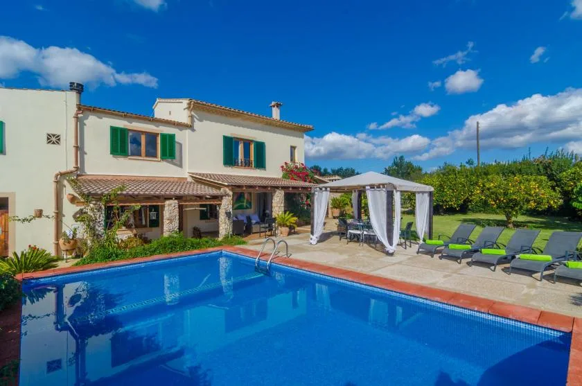 Una piscina junto a una casa de dos plantas, con asientos y una zona de comedor sombreada.