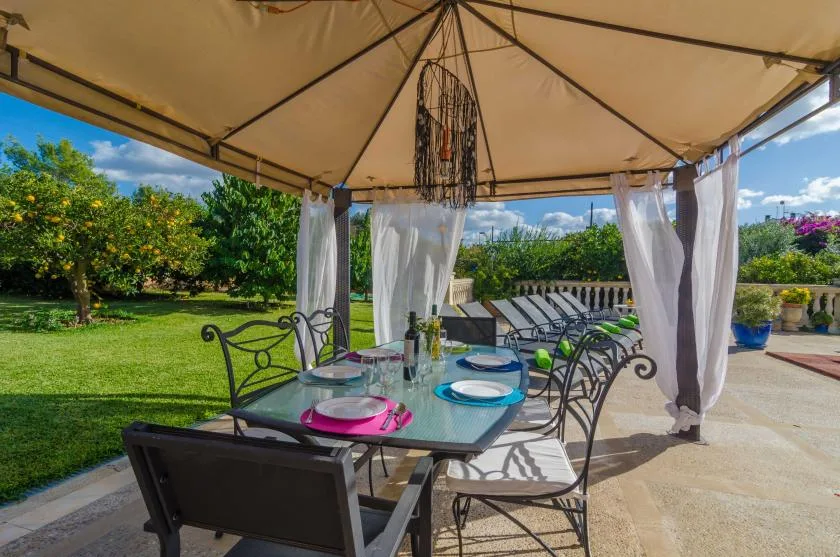 Una zona de comedor al aire libre está bajo un toldo, con un jardín al fondo.