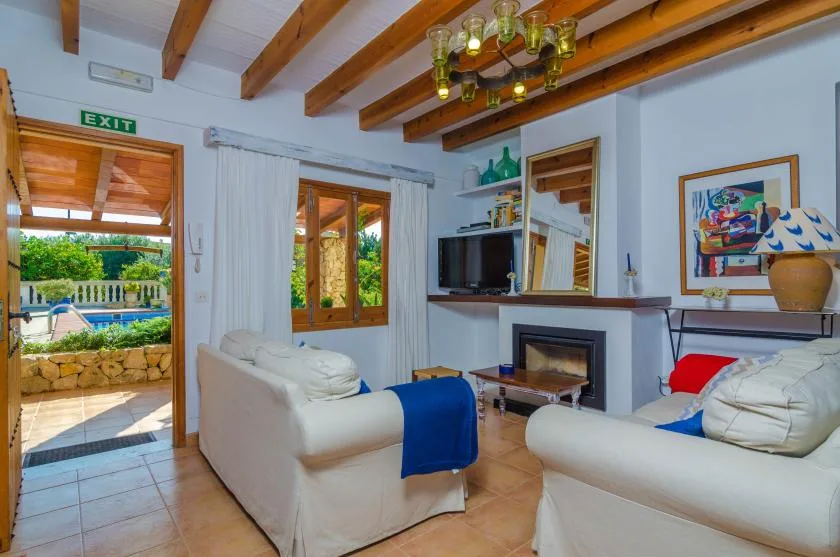 Una sala de estar con asientos claros, una chimenea y una puerta abierta al patio.