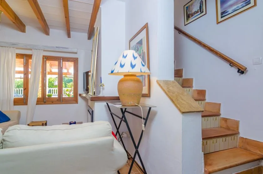 Una sala luminosa con asientos blancos, ventanas de marco de madera y una escalera.