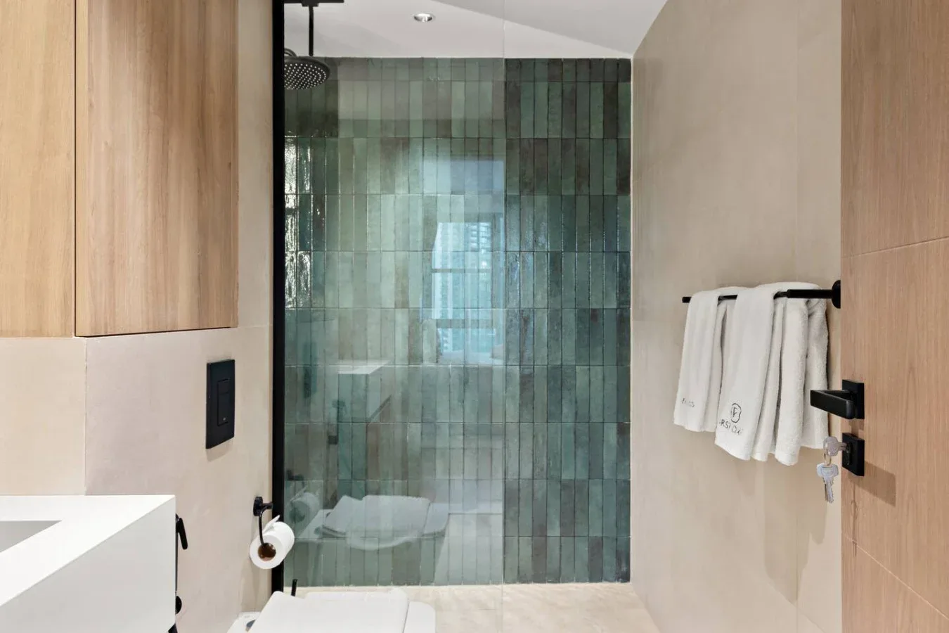 Un baño moderno con ducha de vidrio y paredes de azulejos verdes.