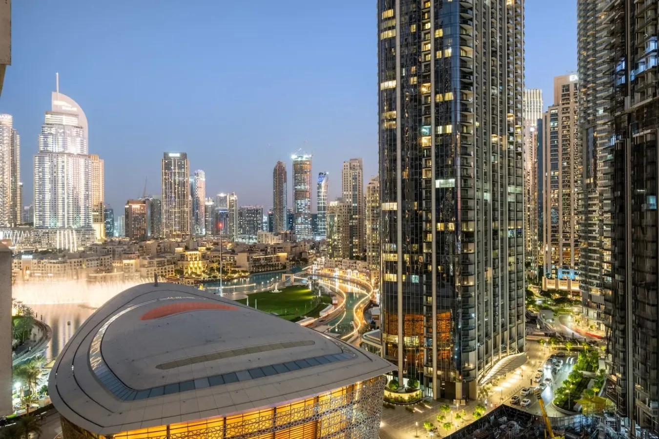 Horizonte urbano al anochecer, con edificios iluminados y una estructura de techo curvo.