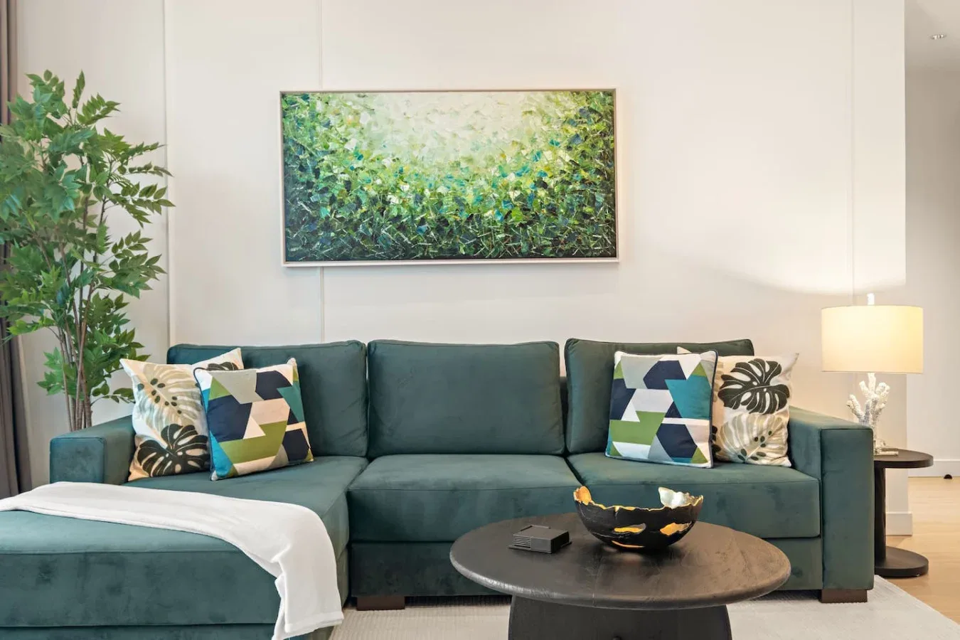 Una sala de estar con un sofá verde azulado, cojines coloridos y un cuadro enmarcado.