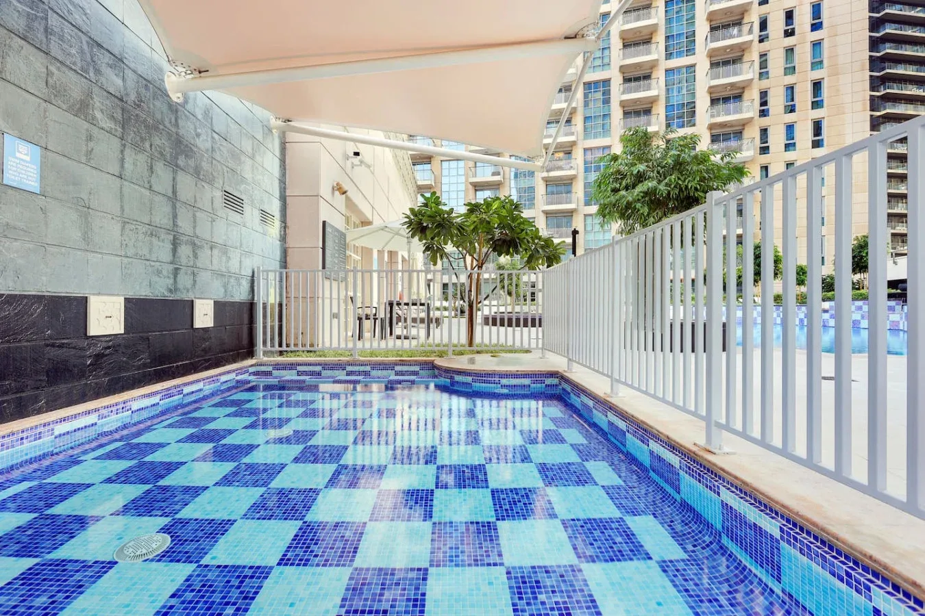 Una pequeña piscina exterior con suelo de azulejos azules está junto a una barandilla blanca.