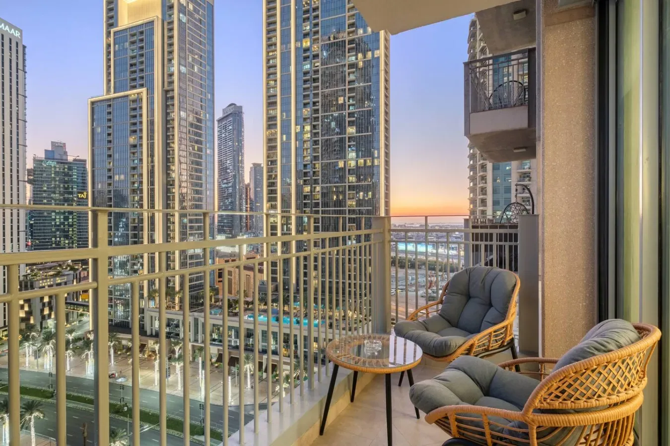 A balcony seating area overlooks high-rise buildings and a city skyline at sunset.