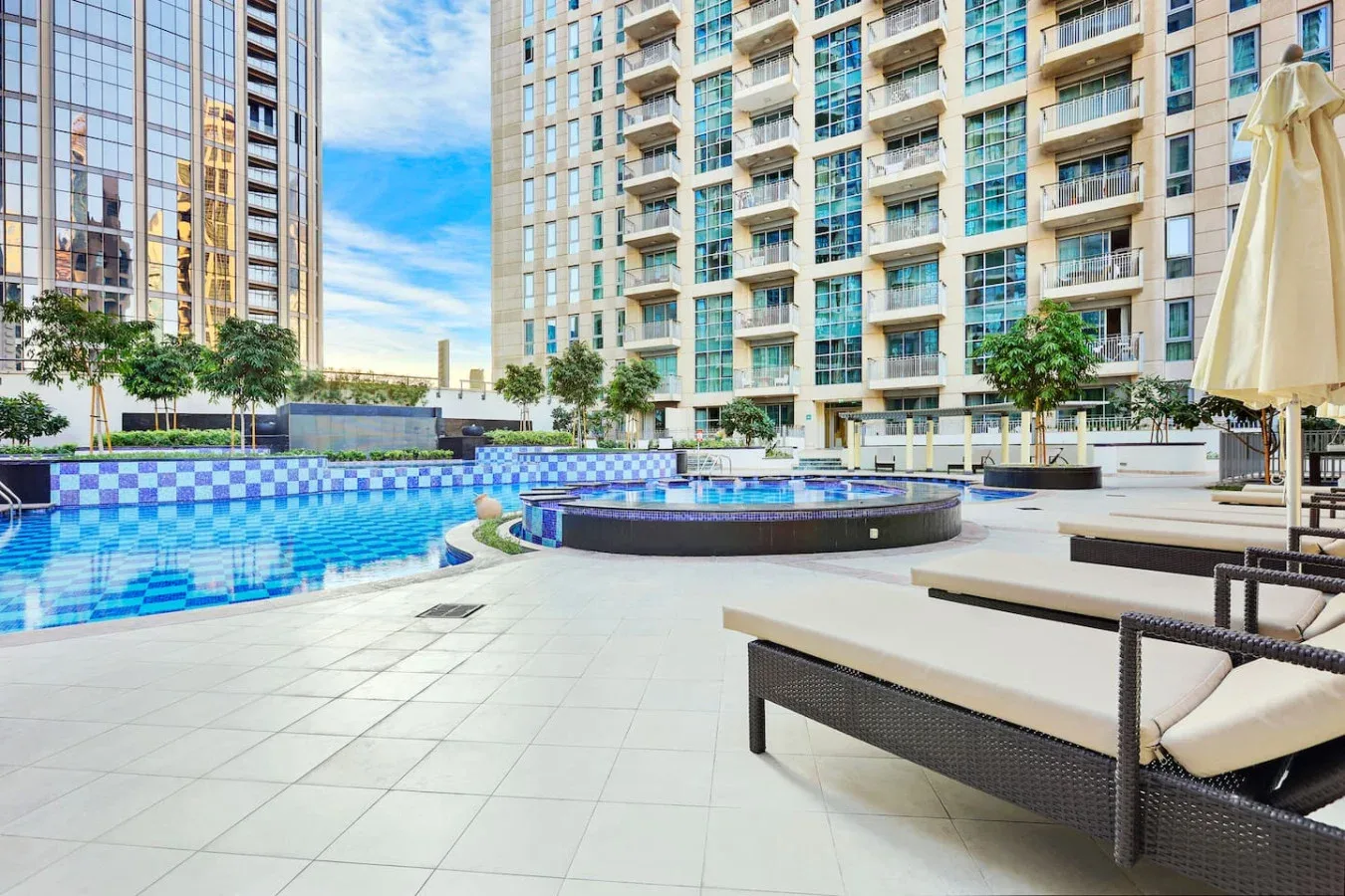 Una piscina al aire libre y un spa circular están junto a un edificio residencial alto.