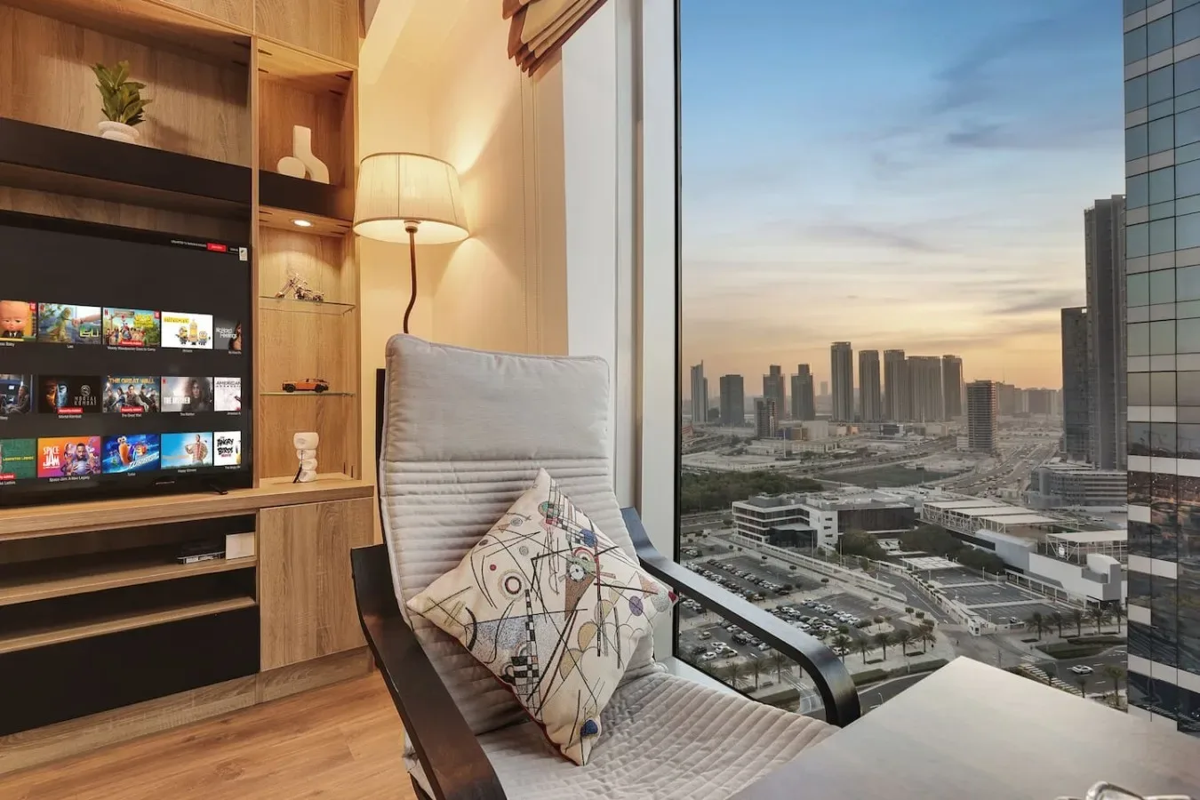 Una zona de estar junto a una ventana de piso a techo da a un horizonte urbano al anochecer.