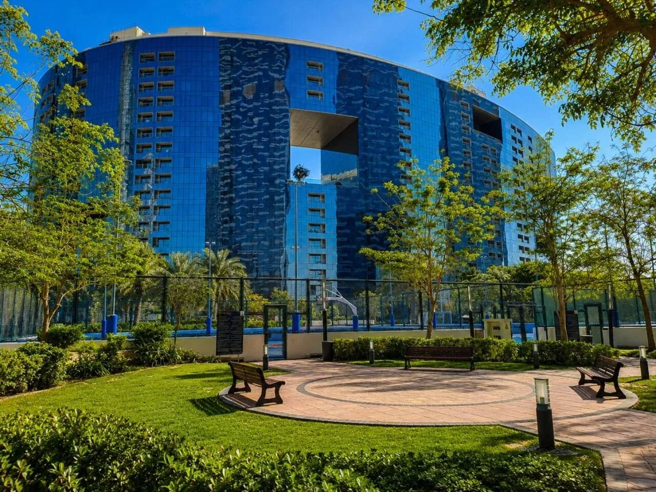 Un patio ajardinado al aire libre con bancos y un edificio azul curvo al fondo.