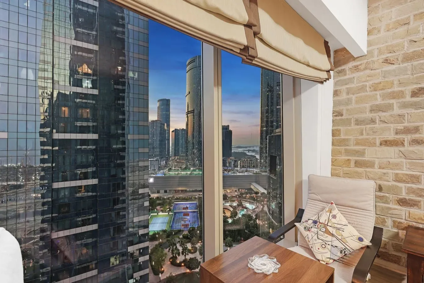 Una zona de estar junto a la ventana ofrece vistas al perfil urbano, con una mesa pequeña al lado del asiento.