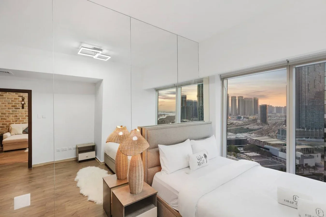 Un dormitorio luminoso con una cama junto a grandes ventanales con vistas a la ciudad.
