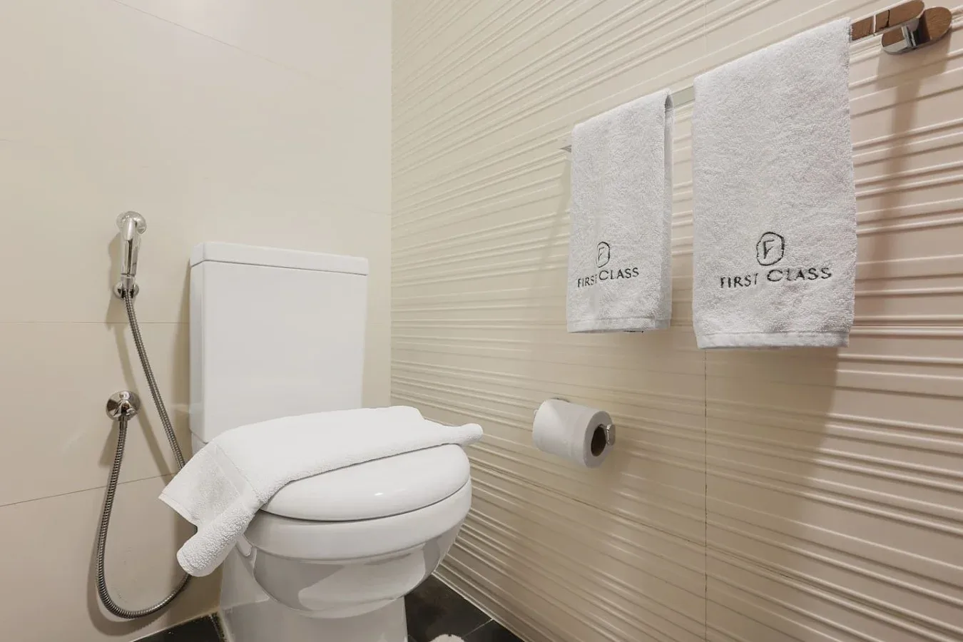 Un baño con inodoro, ducha de mano y toallas colgadas.