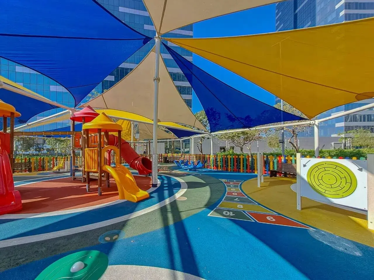 Un colorido parque infantil al aire libre con toboganes bajo grandes toldos.