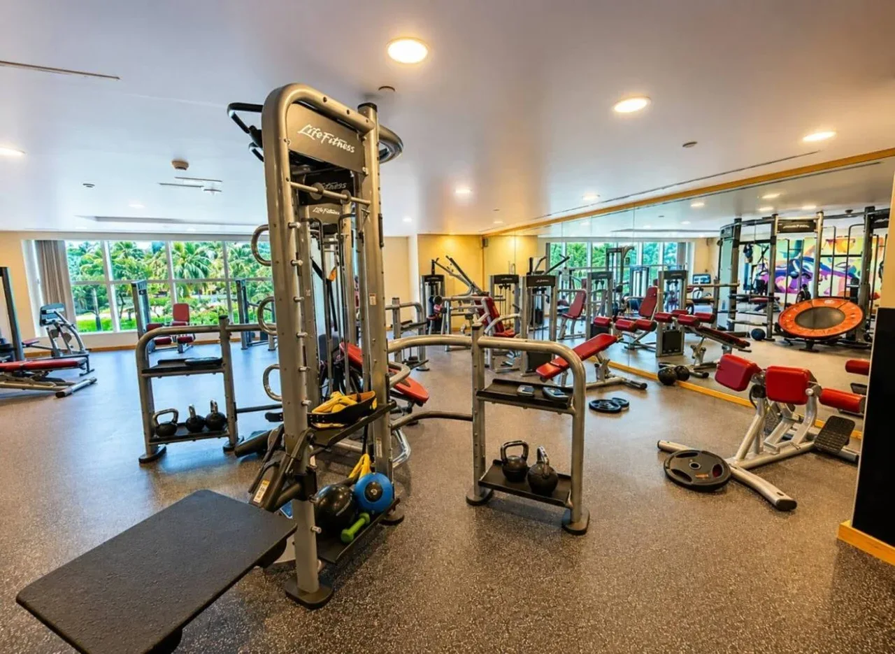Una sala de fitness con máquinas de pesas, bancos y paredes con espejos.