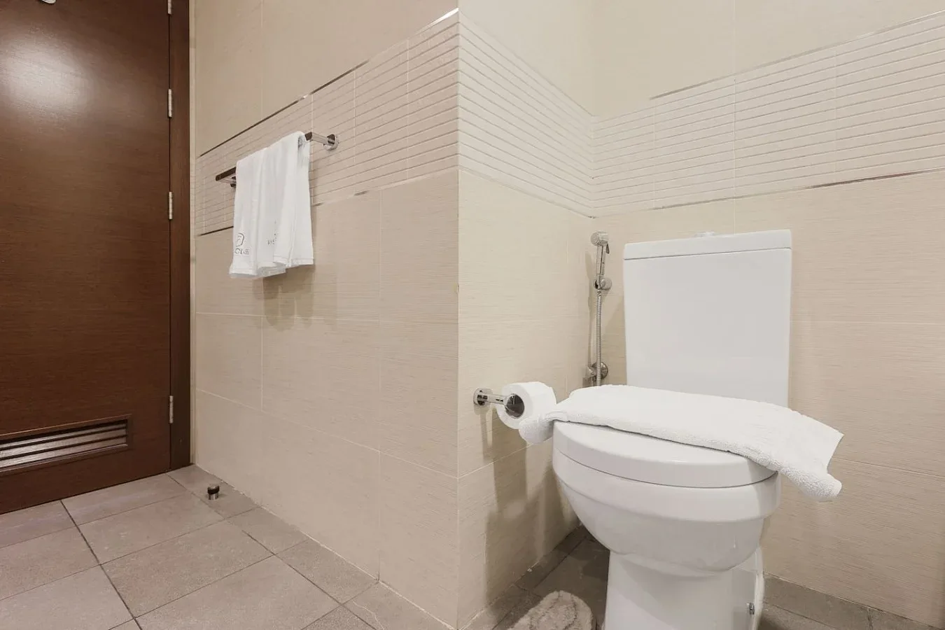 Un baño con un inodoro y una toalla blanca colgada en la pared de azulejos.