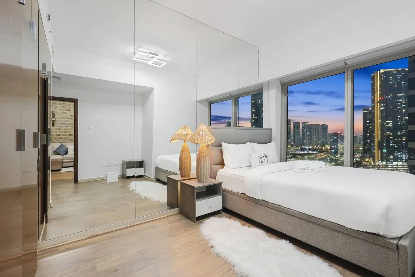 Un dormitorio luminoso con una cama grande junto a ventanales que dan a edificios de la ciudad.