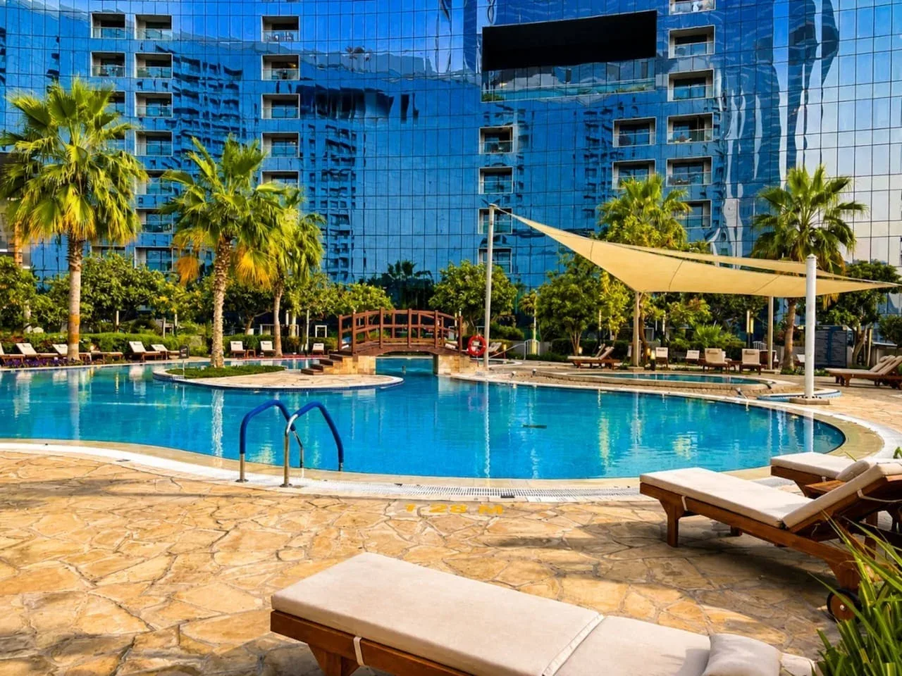 Una piscina al aire libre está junto a un moderno edificio con fachada de vidrio.