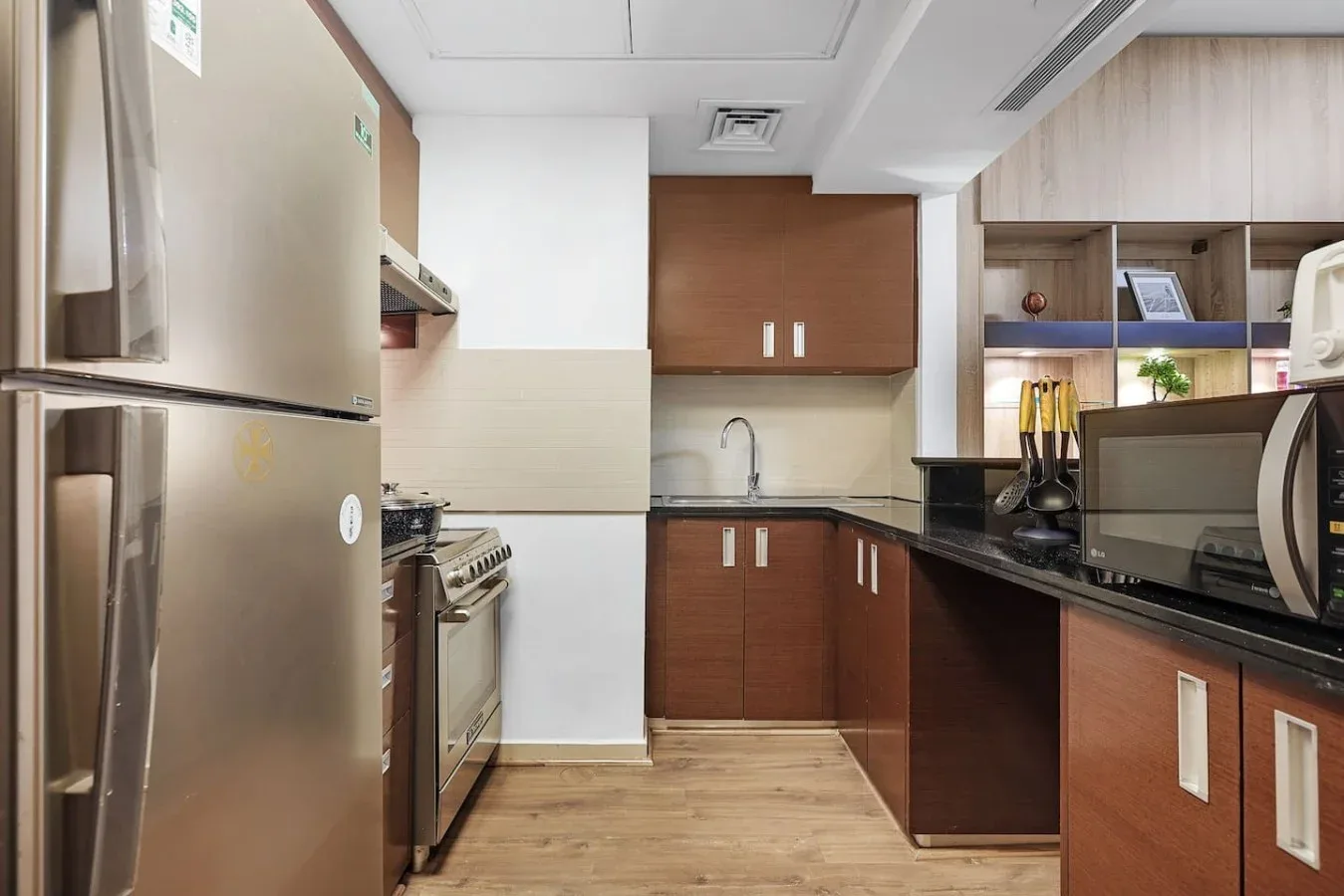 Una cocina compacta con gabinetes de madera, electrodomésticos de acero inoxidable y una encimera oscura.