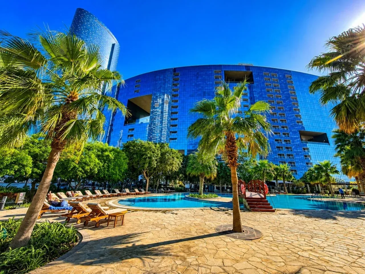 Una piscina y tumbonas están frente a un edificio de vidrio azul.