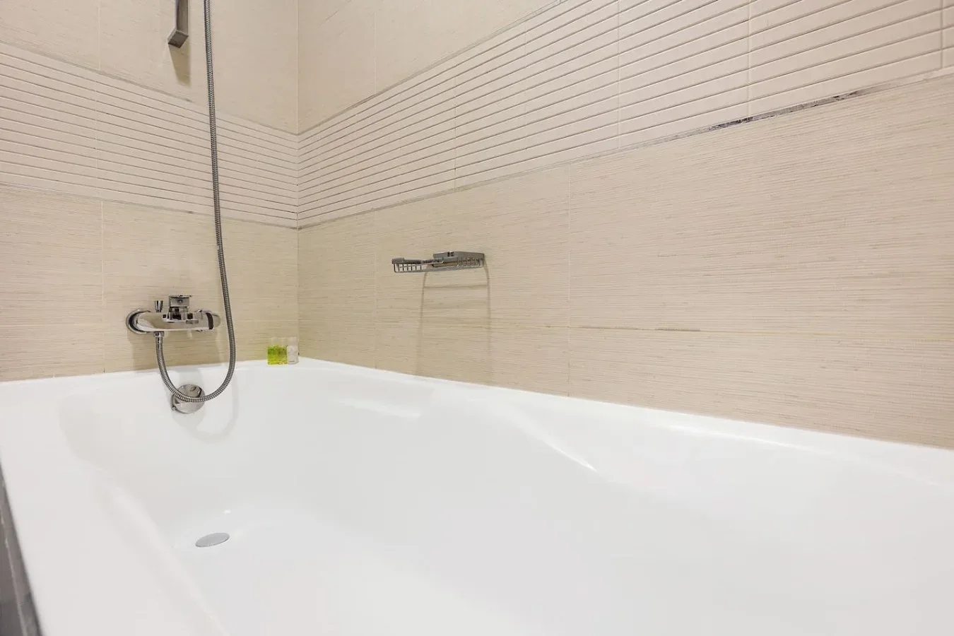 Una bañera está junto a paredes de azulejos beige con una ducha montada en la pared.