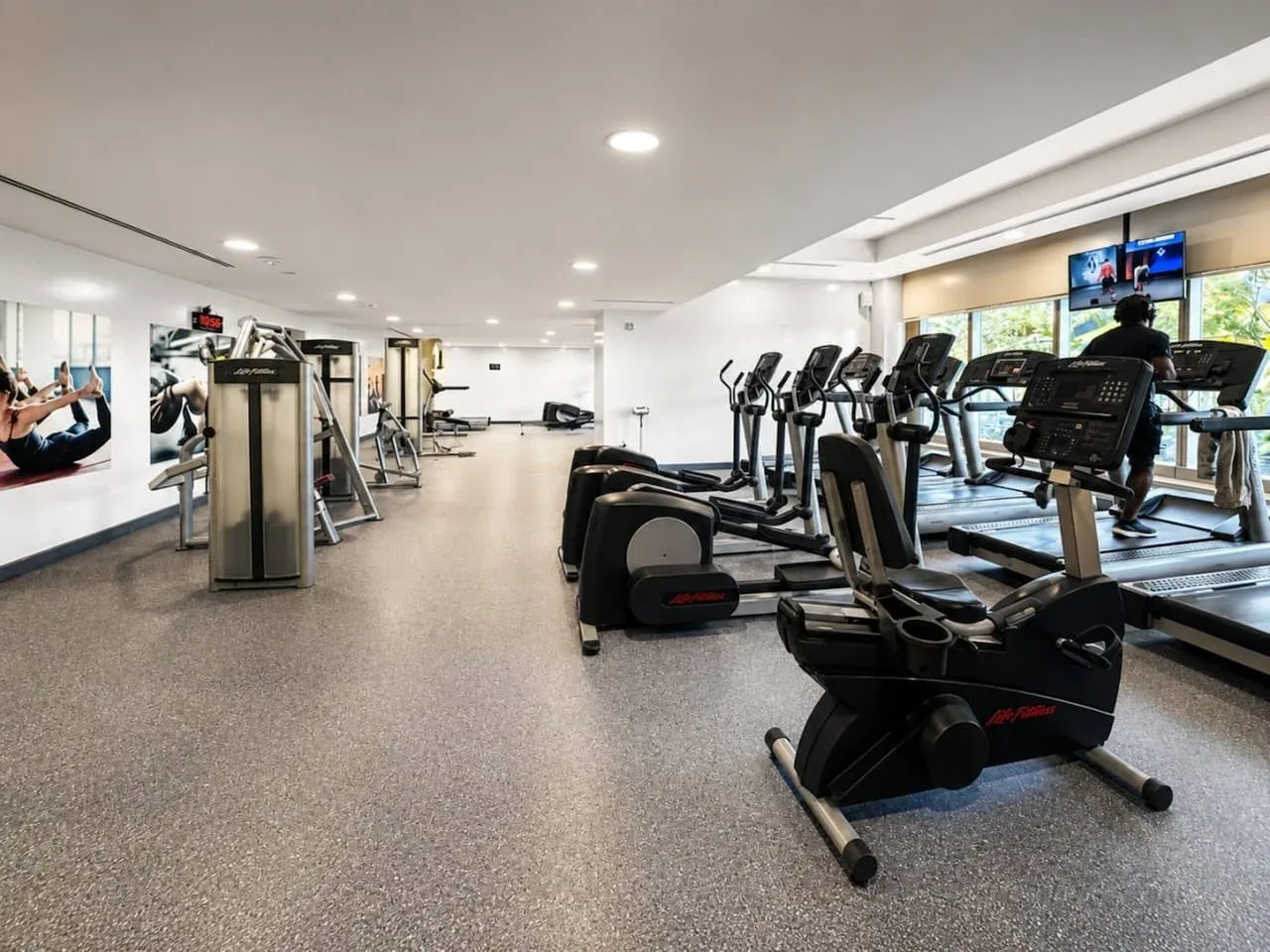 Un gimnasio luminoso con máquinas de ejercicio y equipos cardiovasculares distribuidos por la sala.