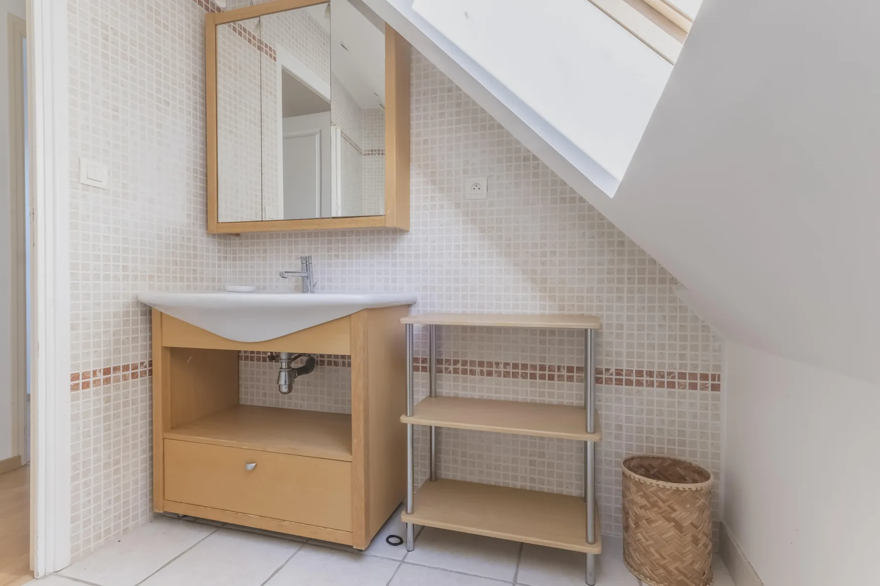 A bathroom with a vanity, open shelving, and a sloped skylight.