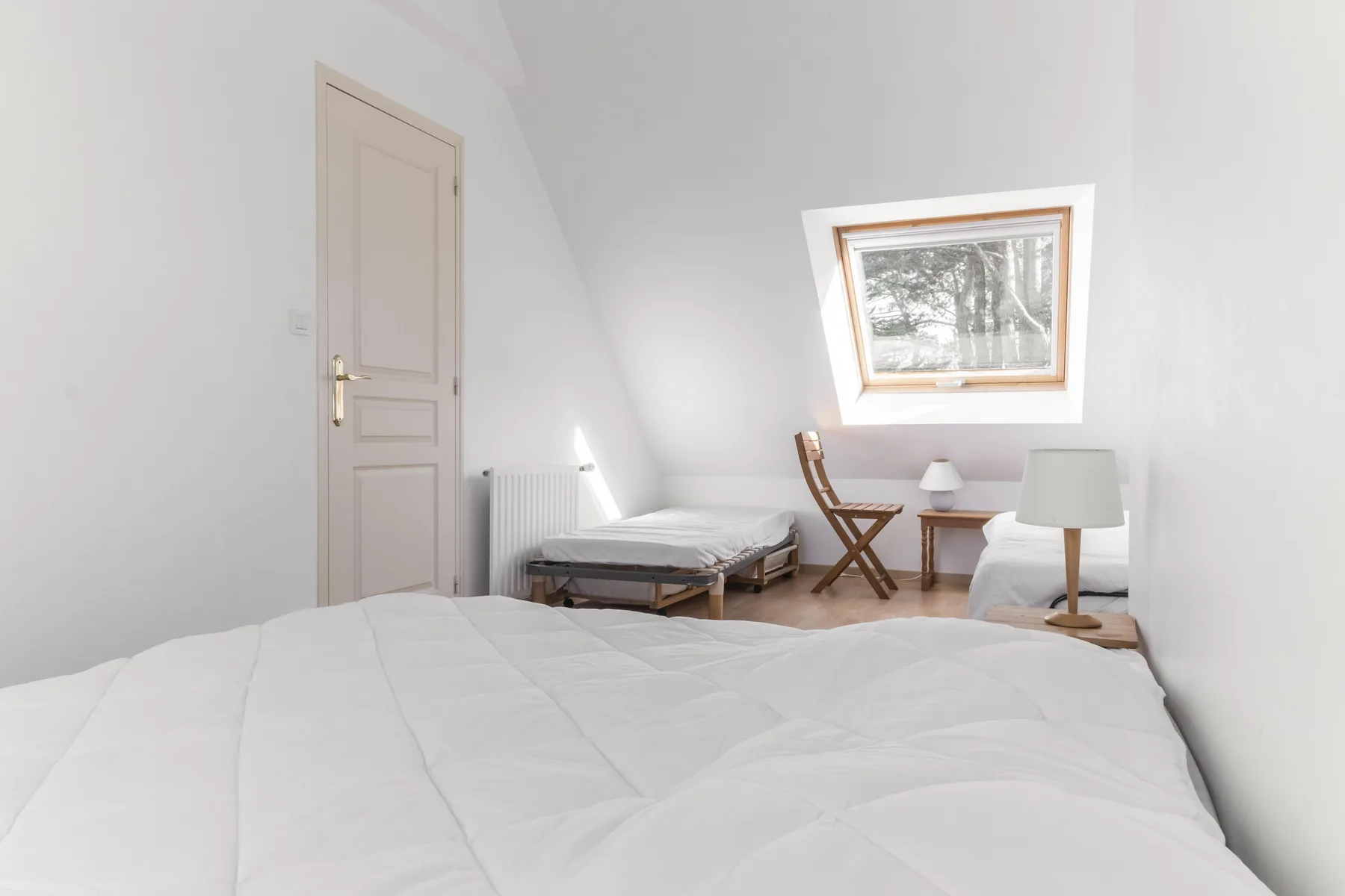 A bright bedroom with beds, a small table, and a window.