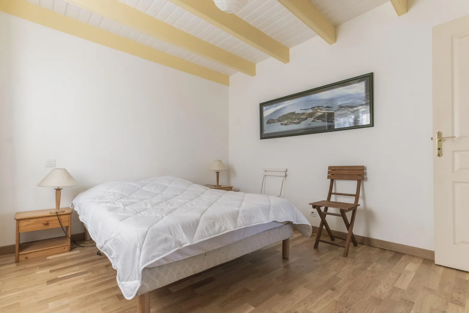 A bright bedroom with a double bed and a framed landscape picture.