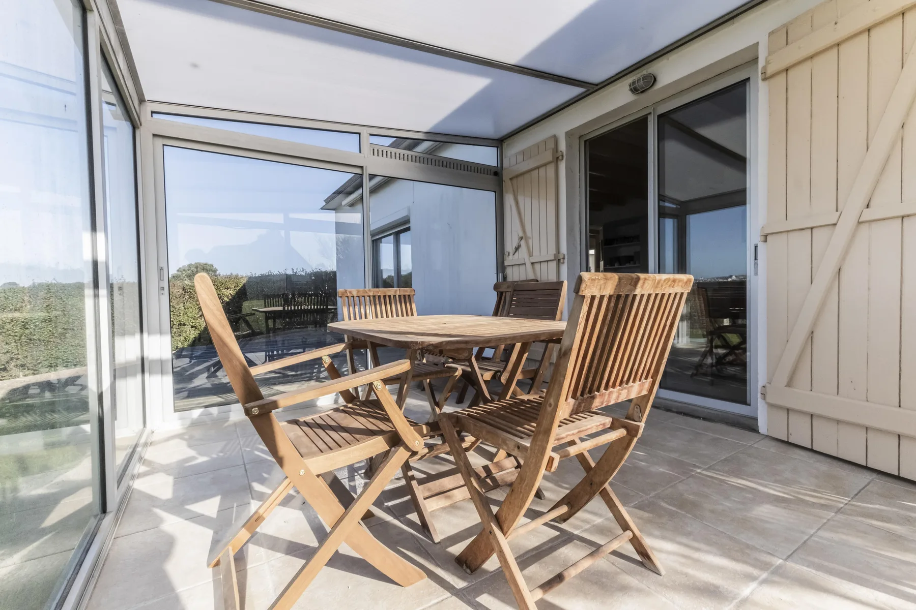 A glass-enclosed patio with a wooden dining table and seating.