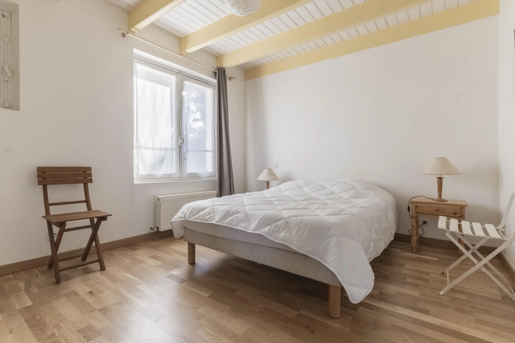 A bright bedroom with a bed, a window, and simple furnishings.