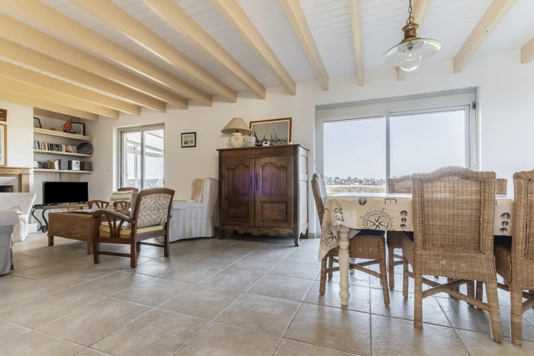 A bright dining and living area with a table beside large windows.