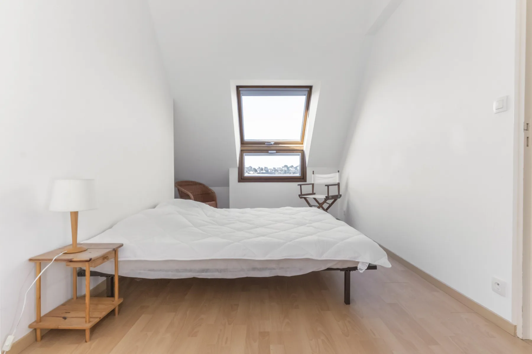 A bright bedroom with a bed beneath a sloped ceiling and skylight.