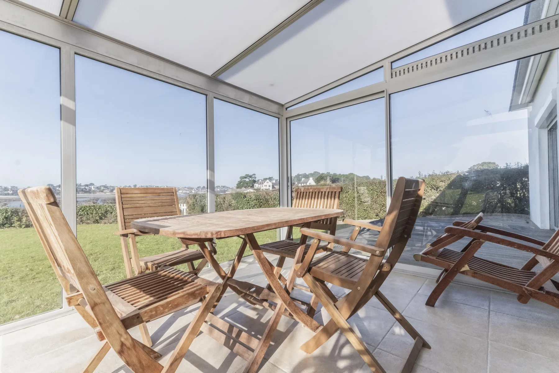 A glass-enclosed dining area with a wooden table and outdoor seating.
