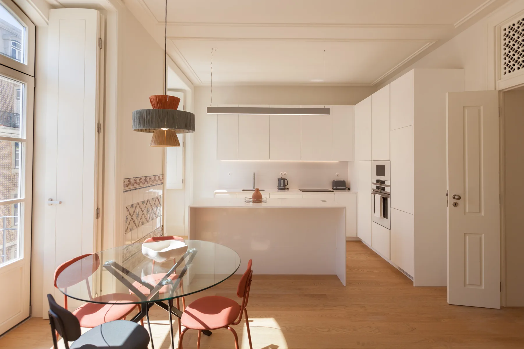 Una luminosa cocina con comedor, mesa de vidrio y asientos rojos.