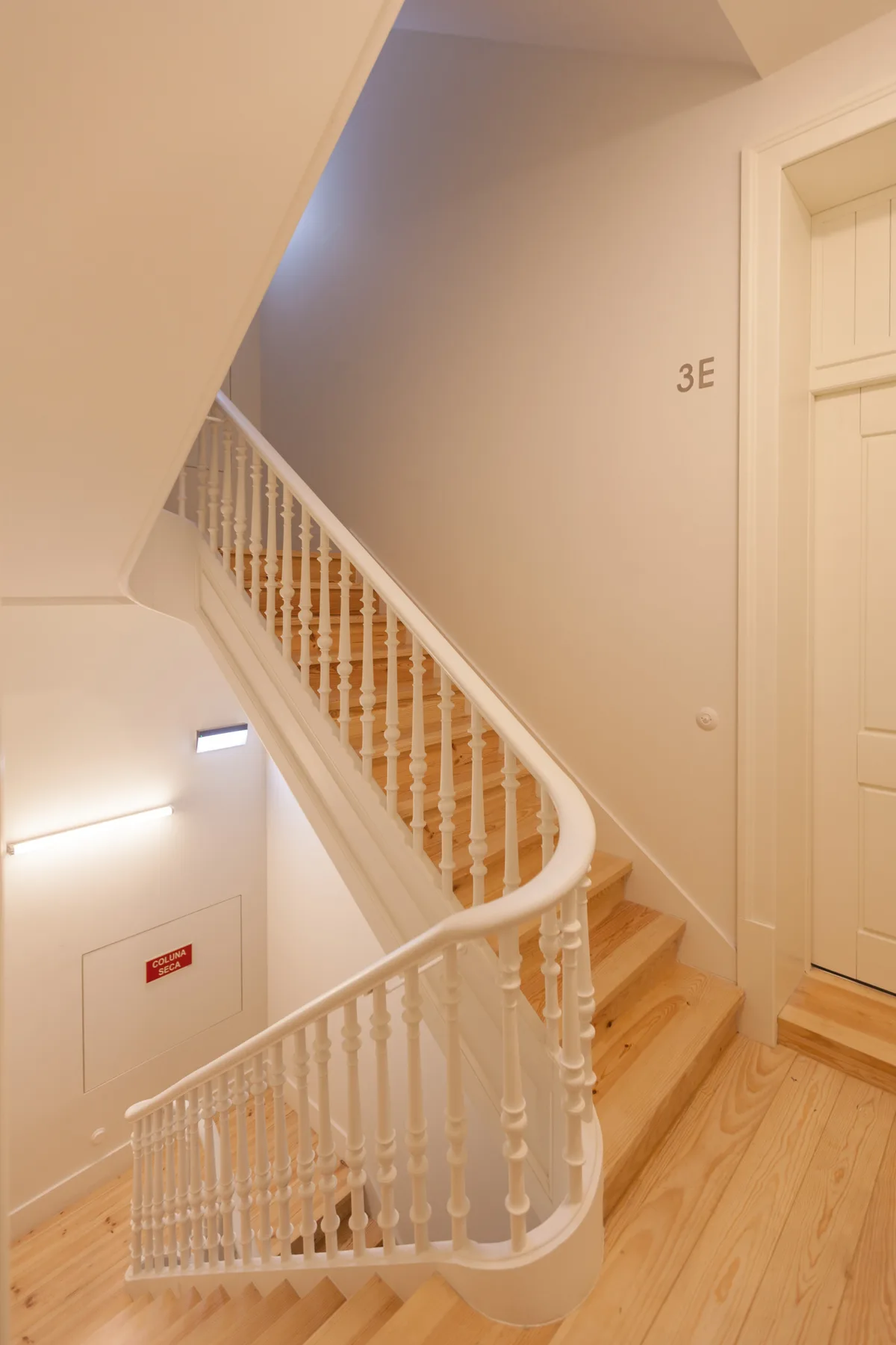 Una escalera interior con barandillas blancas y escalones de madera clara.