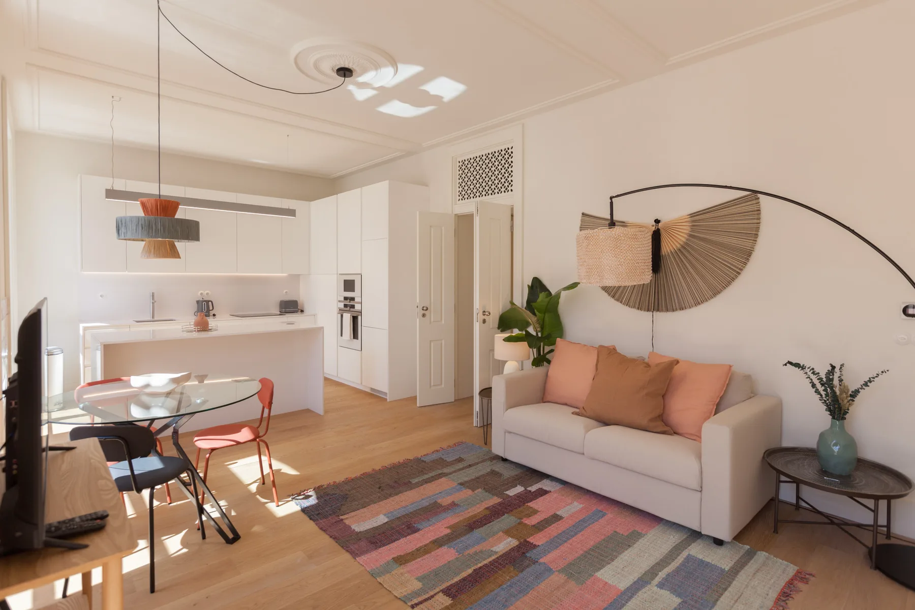 Una luminosa sala de estar con sofá, alfombra colorida y cocina abierta.