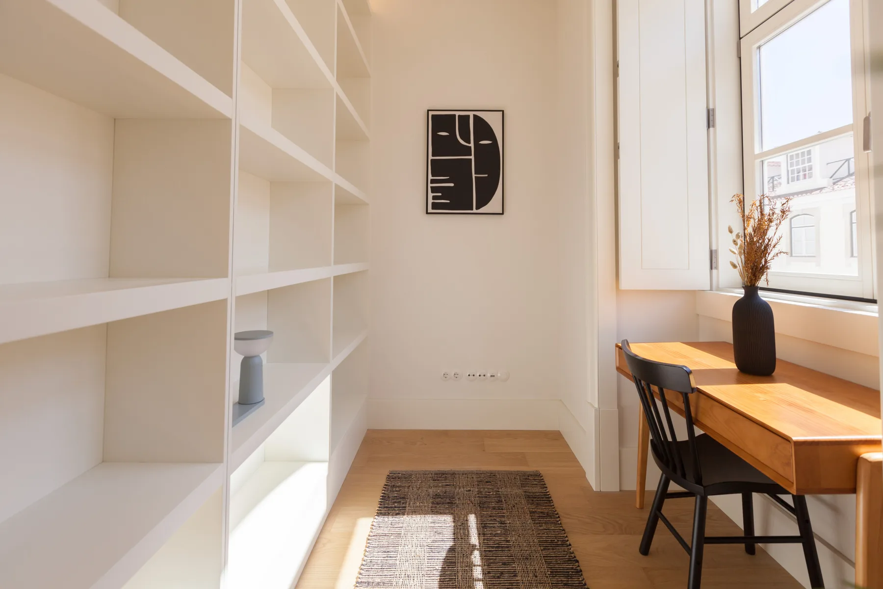 Un rincón de estudio luminoso con estanterías, escritorio y ventana.