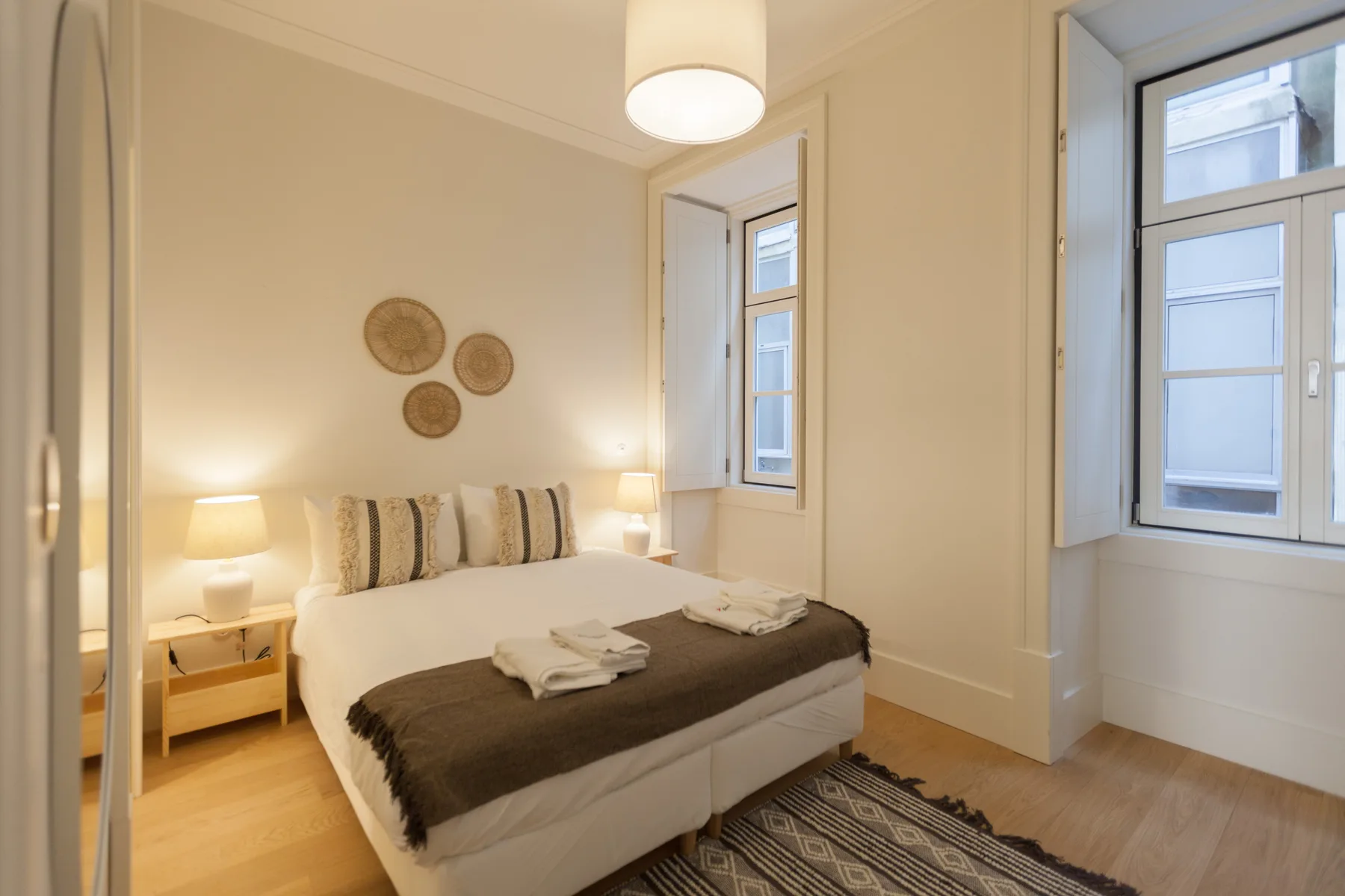 Un dormitorio con una cama, toallas dobladas y dos ventanas.