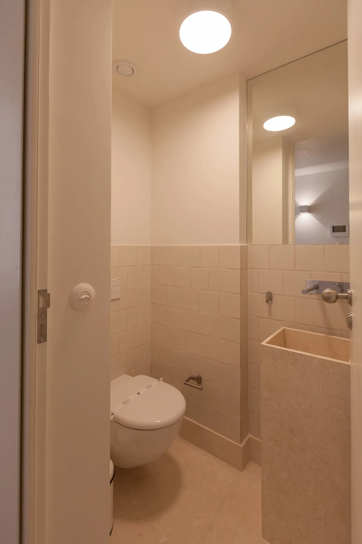 Un baño con un inodoro, paredes alicatadas y un espejo grande.