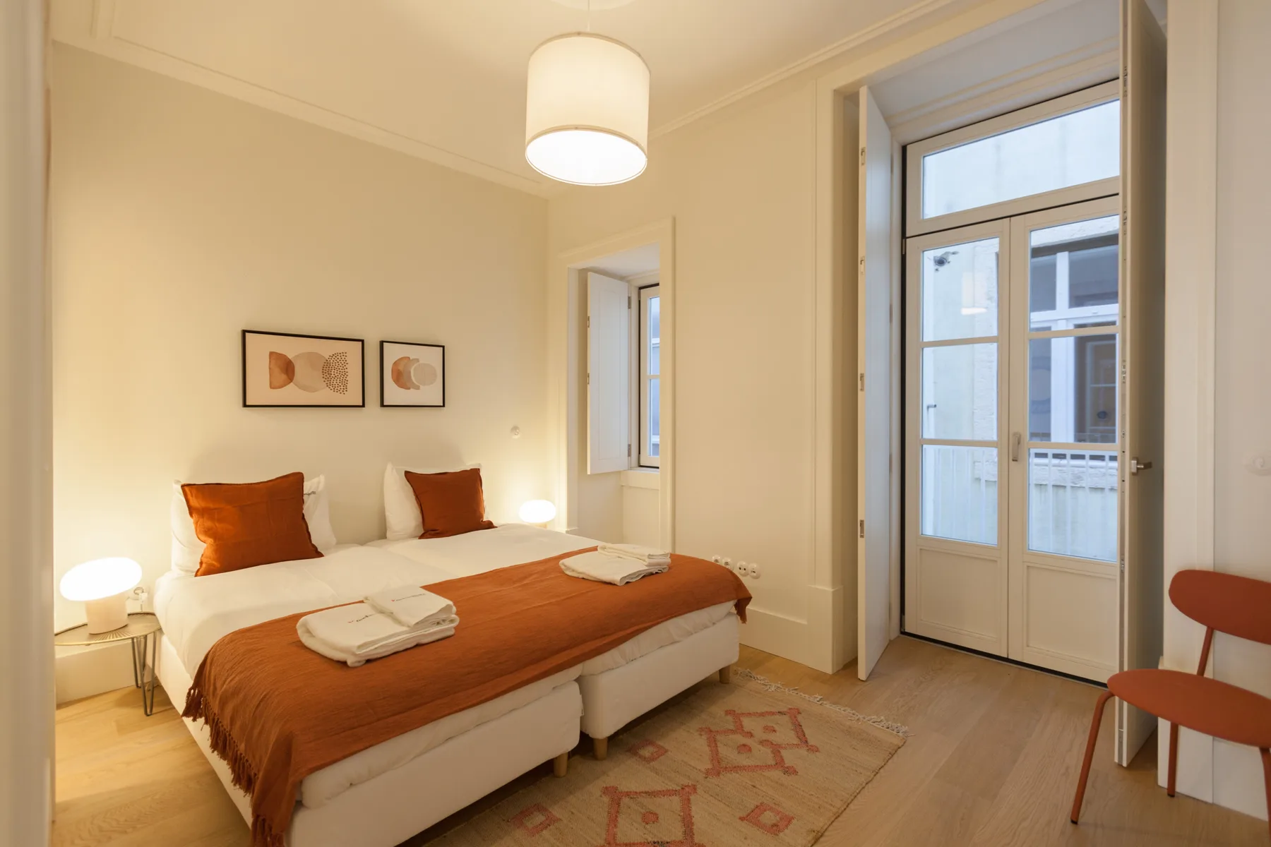 Dormitorio con cama doble, ropa de cama color óxido y una puerta acristalada al balcón.