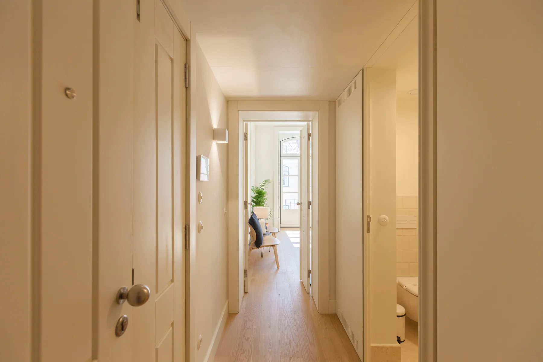 Un pasillo luminoso conduce a una habitación con ventana y asientos.