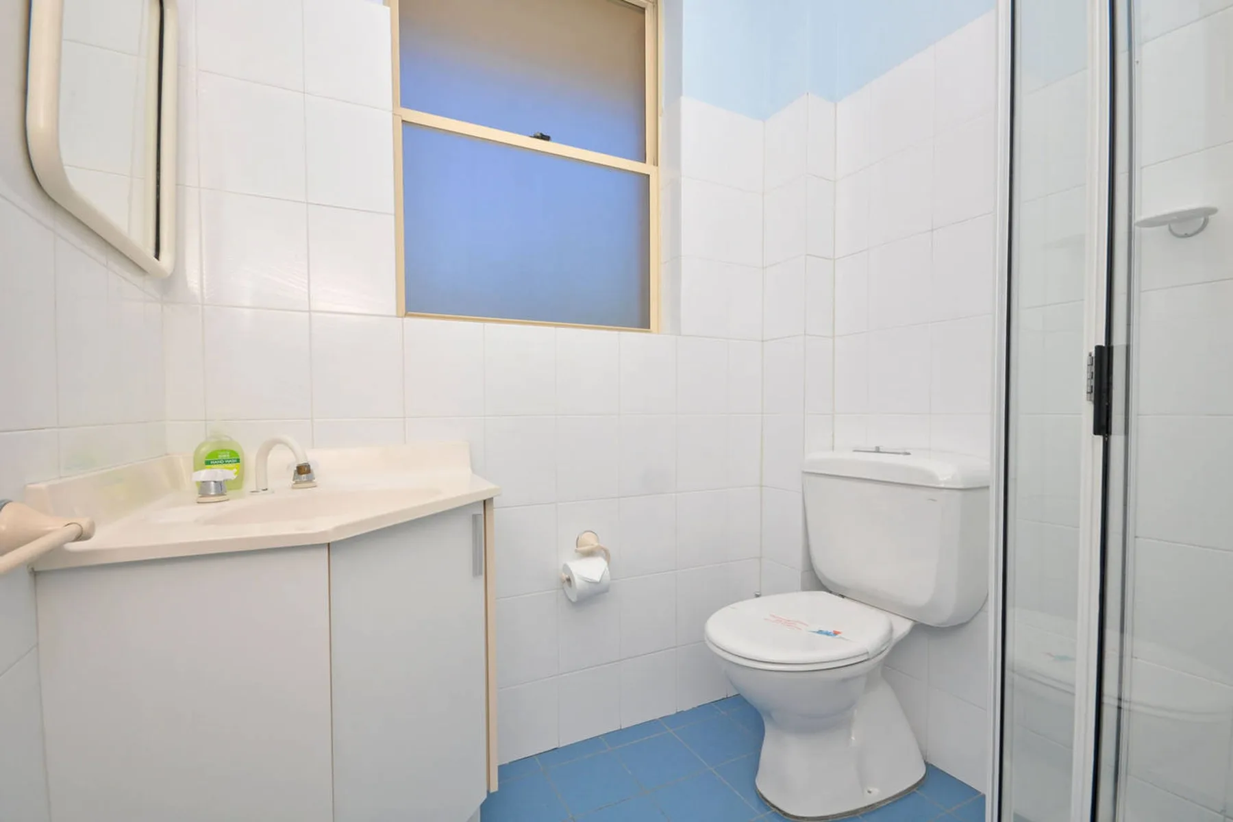 Un baño alicatado con lavabo, inodoro y ducha con mampara de vidrio.