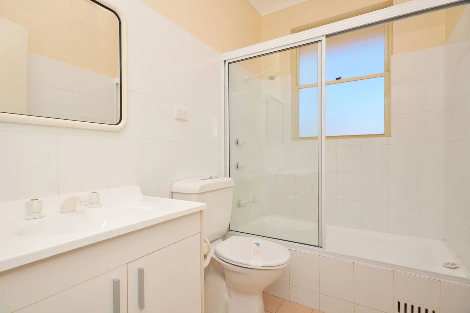 Baño con lavabo, inodoro y bañera tras paneles corredizos de vidrio.
