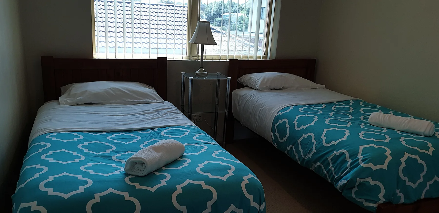 Un dormitorio con dos camas individuales y ropa de cama azul estampada junto a una ventana.