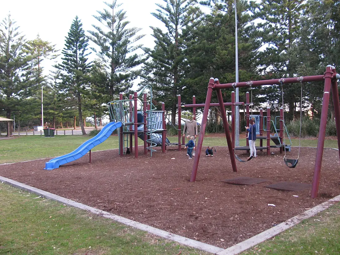 Un parque infantil al aire libre con toboganes y columpios bajo árboles altos.