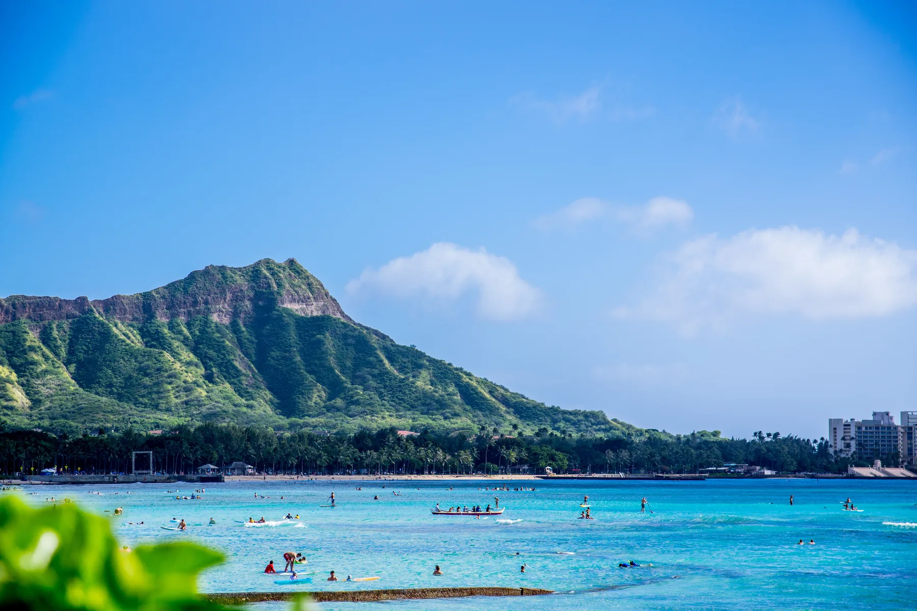 Una playa tropical con bañistas y una montaña verde que se alza tras la costa.