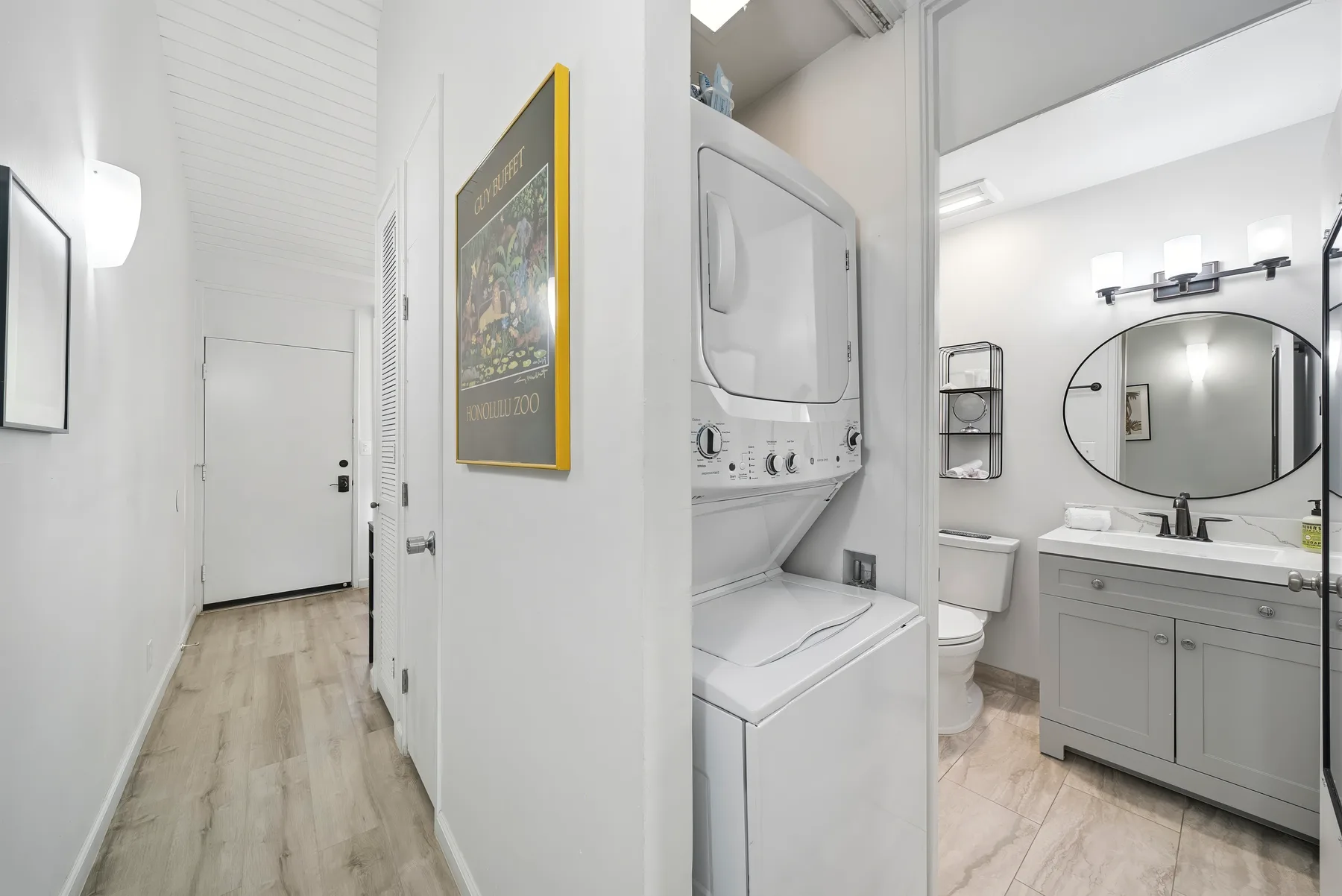 Un pasillo luminoso da a un baño con lavabo y máquinas de lavandería.