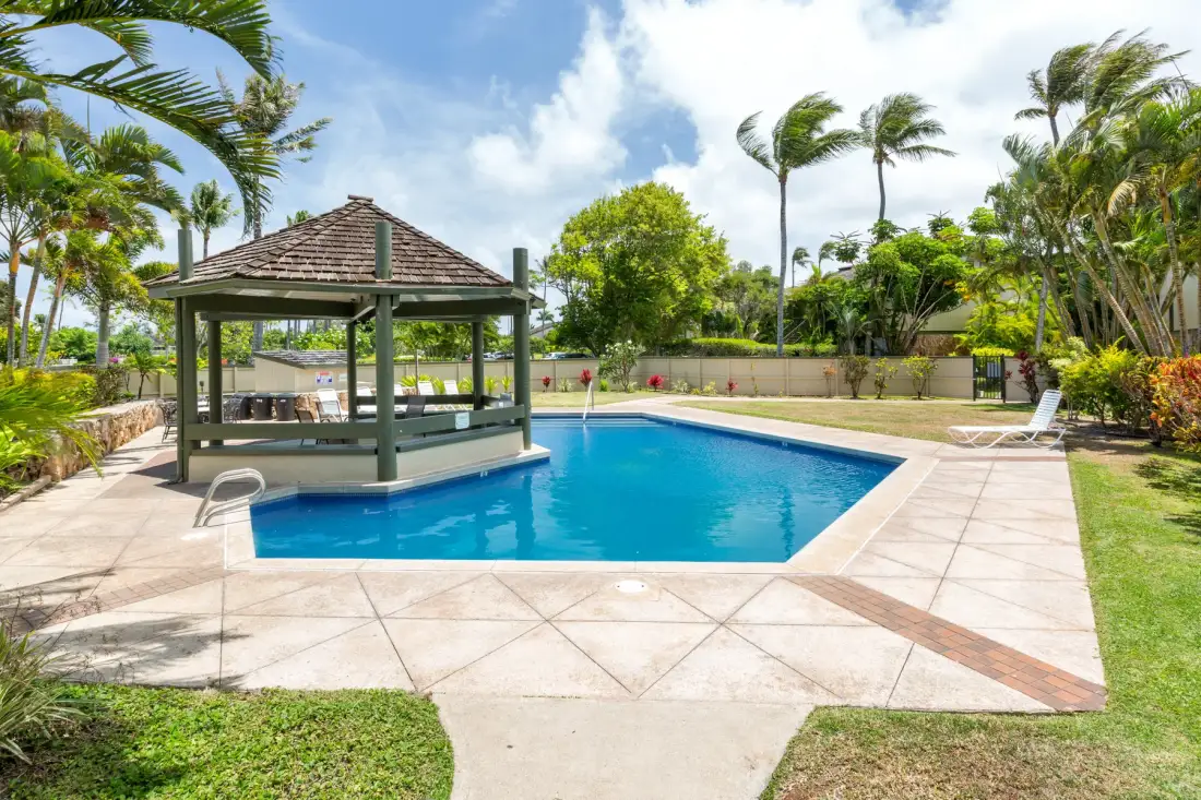 Una piscina al aire libre con un cenador sombreado y palmeras.