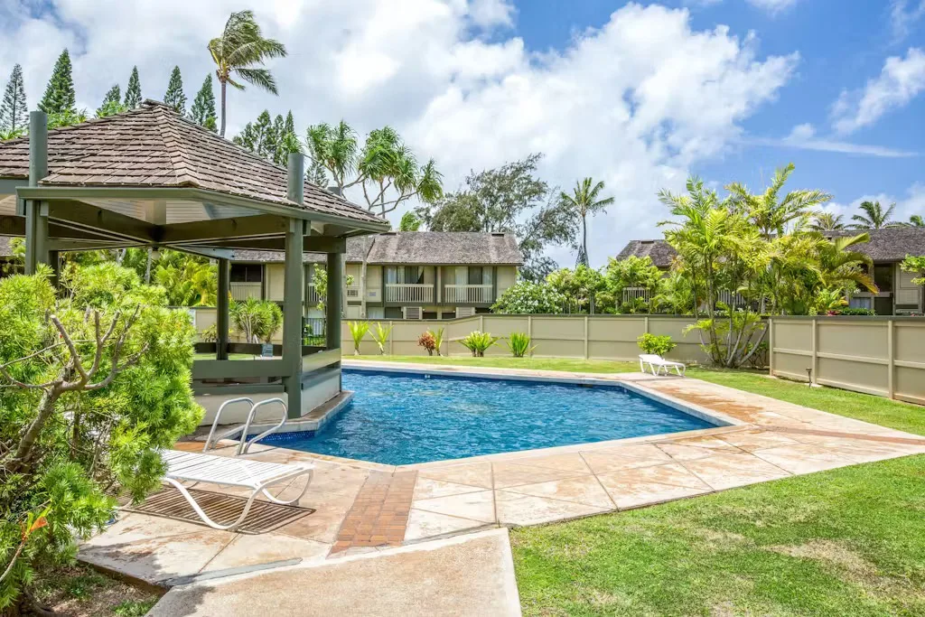 Piscina al aire libre junto a una zona de estar cubierta y jardines.